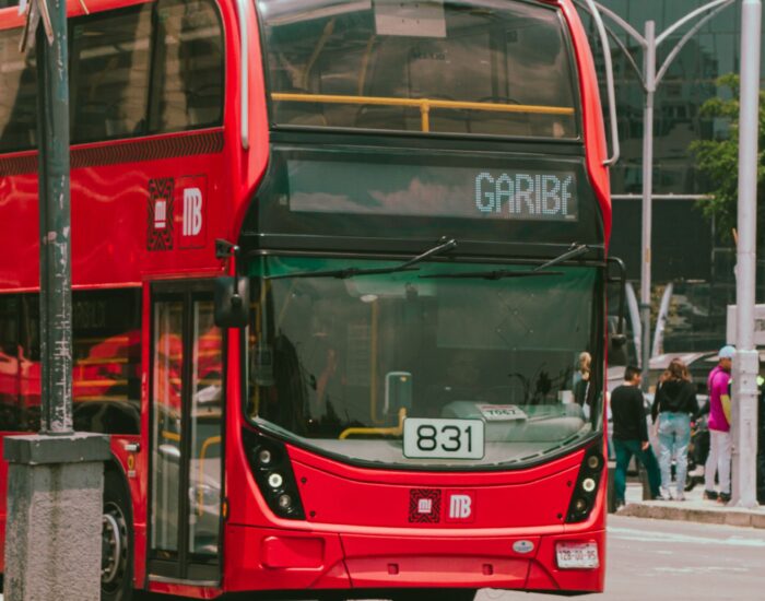 A vibrant red double-decker bus driving on a lively urban street with people.