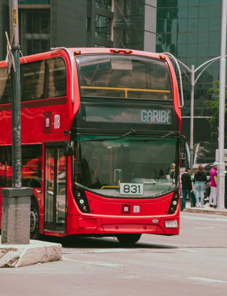 A vibrant red double-decker bus driving on a lively urban street with people.